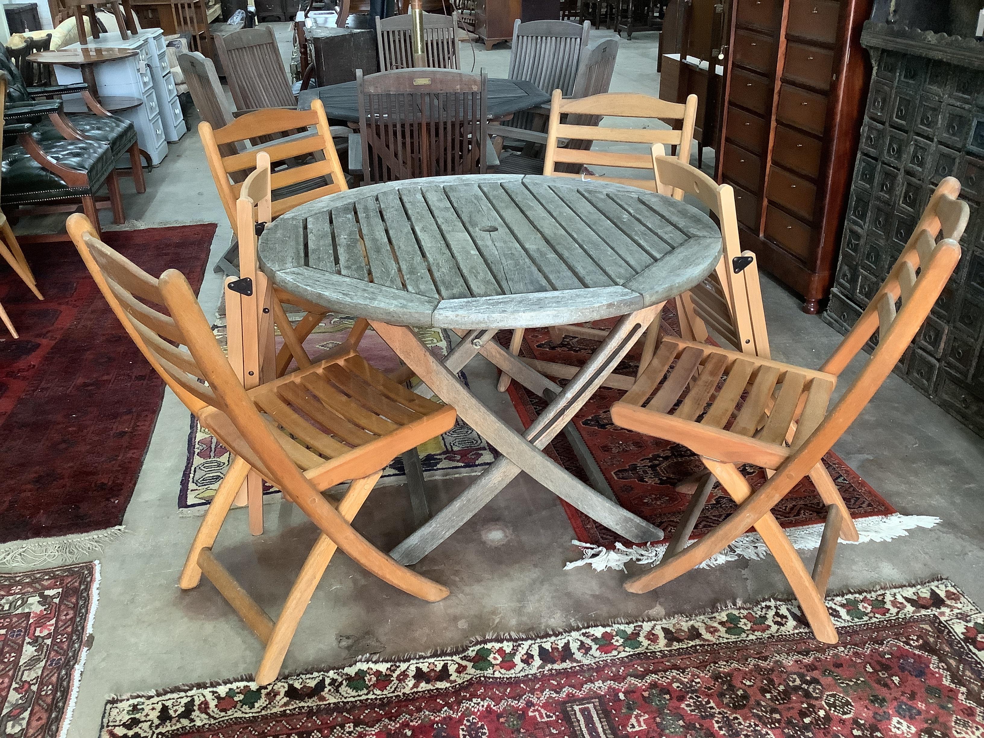 A circular weathered teak garden table, diameter 111cm, height 73cm with four folding hardwood chairs and two other chairs